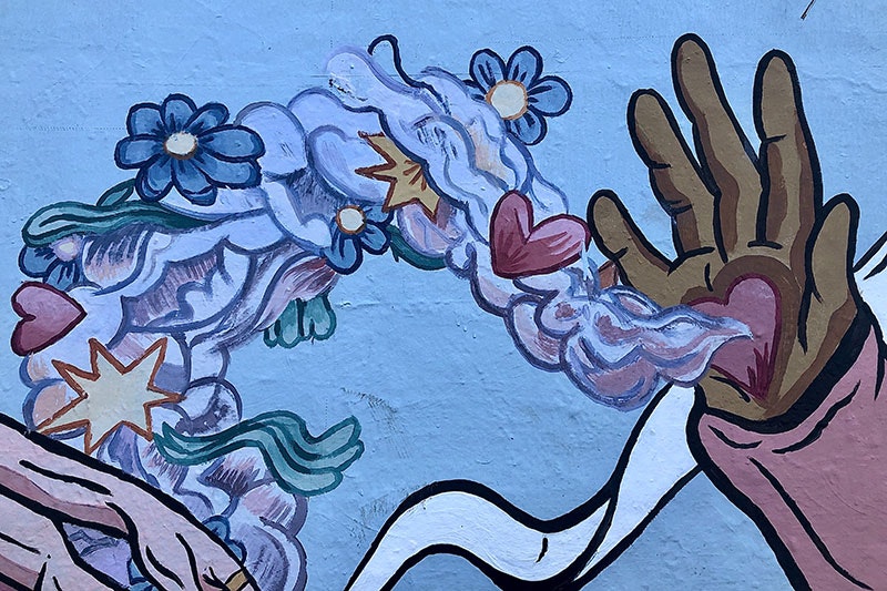 Paintings on a fence of an open hand held up with a love heart on the palm, emitting smoke filled with hearts and flowers