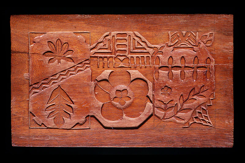 A wooden stamp with flower, leaf, and line patterns carved into it to be used as a pattern to ink onto material.
