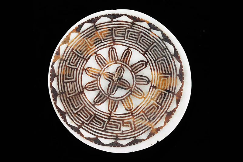 A round disc made of turtle shell that has been carved into a pattern.