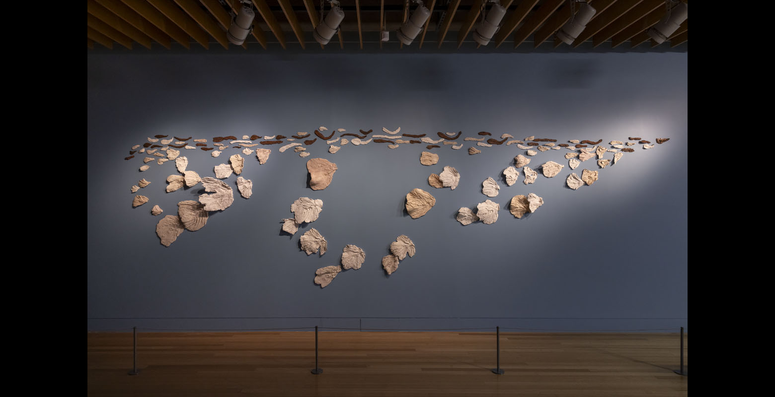 An array of ceramics of all sizes resembling leaves, assembled together on a wall in a pattern that loosely resembles a bird in flight