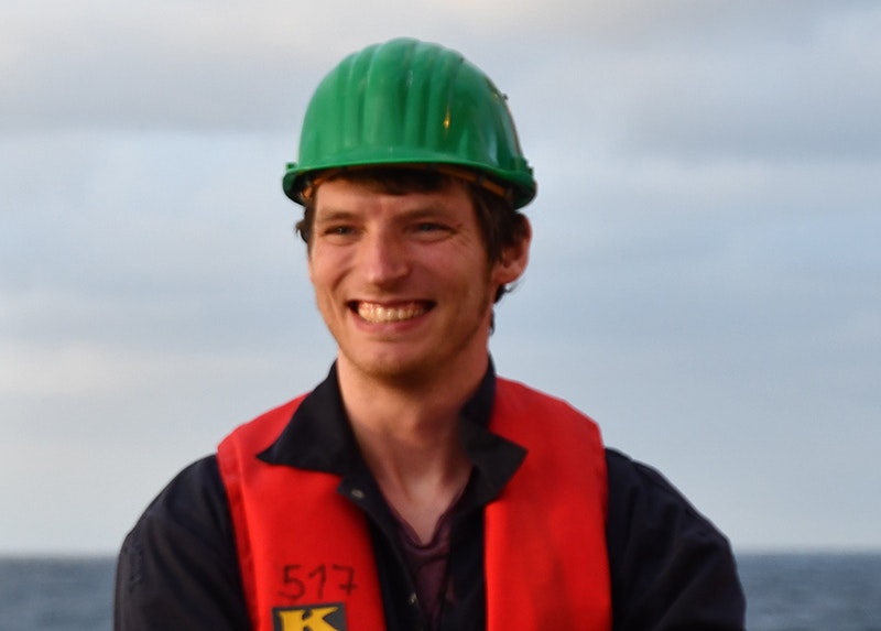 Head and shoulders of a man in a high-vis vest and red hard hat smiling at something off camera