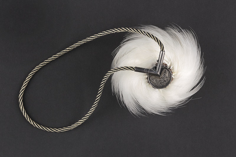 A round ball covered in white feathers with a black and white braided cord attached. There is also