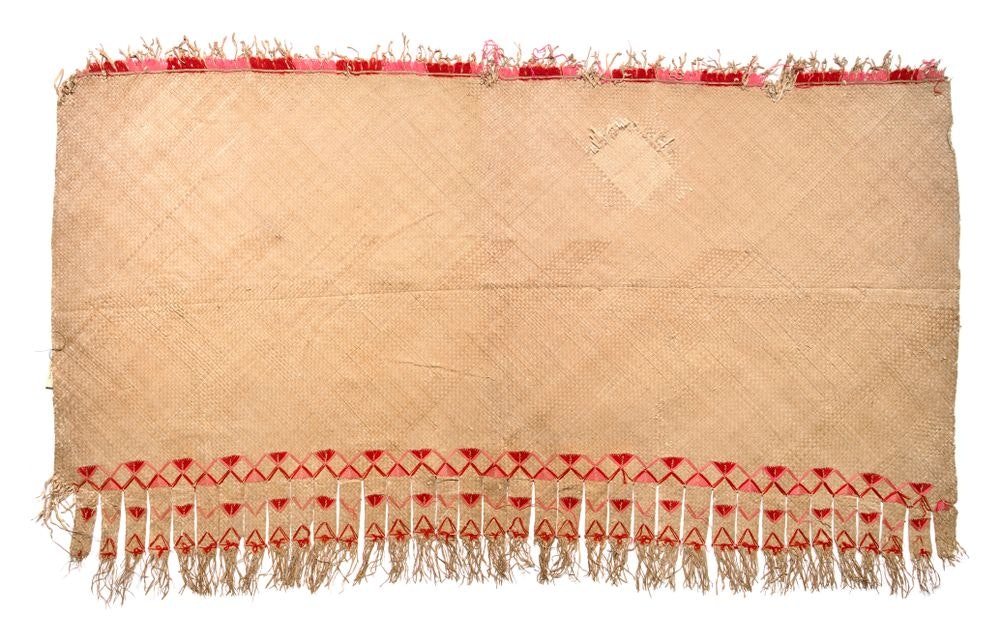 A large woven mat with red trim at the top and red zig-zag patterns at the bottom with long tassles.