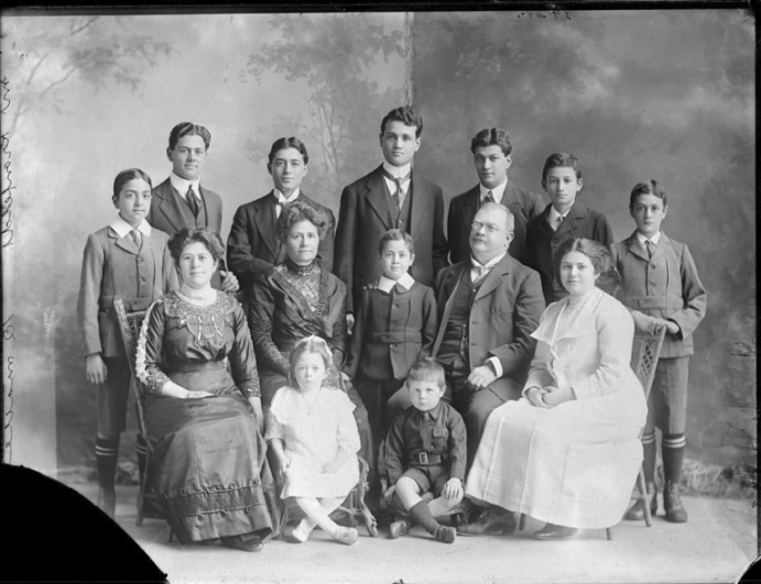 A black and white studio photograph or a large family in between 1910 and 1930