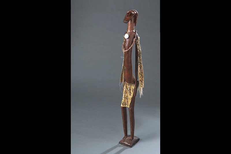 A carved wooden figure with a necklace and breastplate and cloth with designs on it.