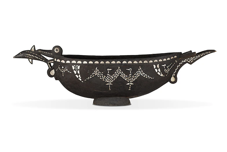 a black wooden bowl shaped a bit like a gravy boat with shell inlaid in patterns on it.