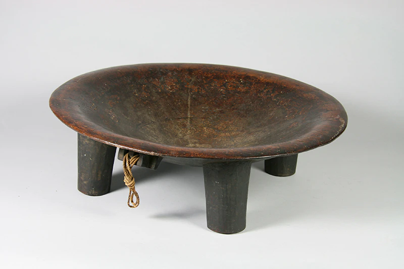 A carved wooden bowl with four wooden legs sitting on a grey background.