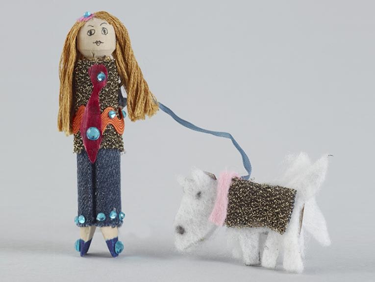 A doll made from a wooden clothes peg accompanied by a dog on a leash made from material.