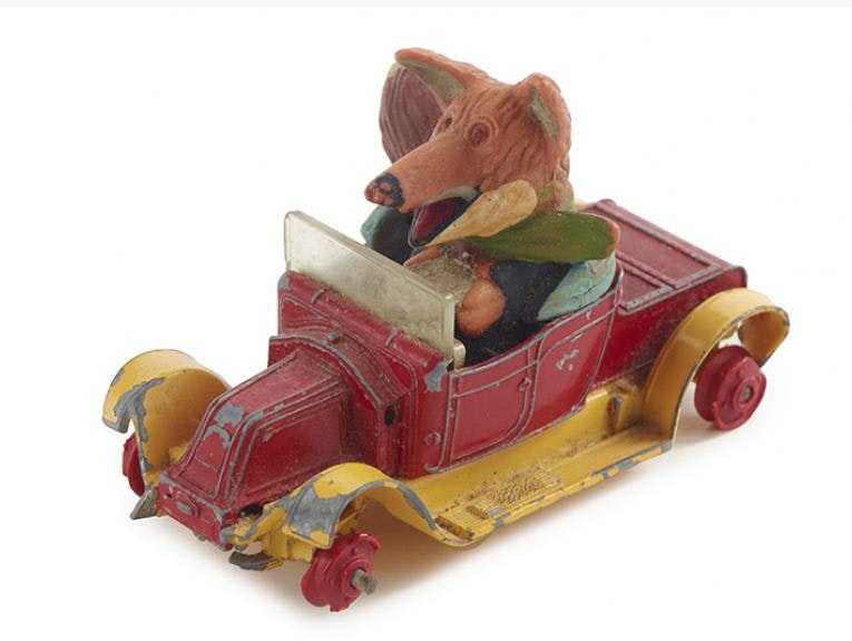 A toy fox dressed in clothing is driving a toy car