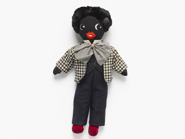 A doll on a light grey background. The doll is dark black and called a golliwog.