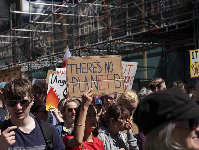 People marching down a street. A young woman holds up a sign that says “There’s no Planet B”