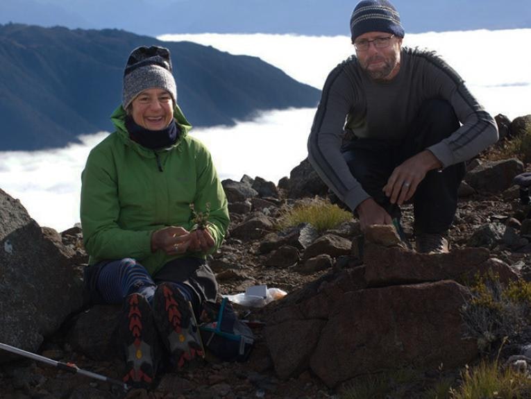 Two people in hiking clothes are sitting on top of a mountain.