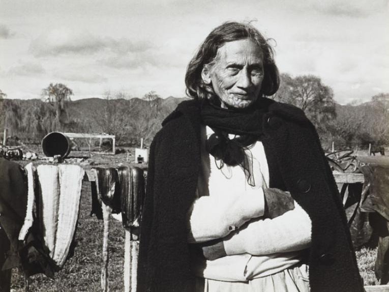 Marti Friedlander. Mere Brown. From the series: The Moko Suite, 1970. Gelatin silver print. Gift of The Gerrard and Marti Friedlander Charitable Trust, 2009. Te Papa, O.033747. A lady with a chin moko stands outside with her arms folded