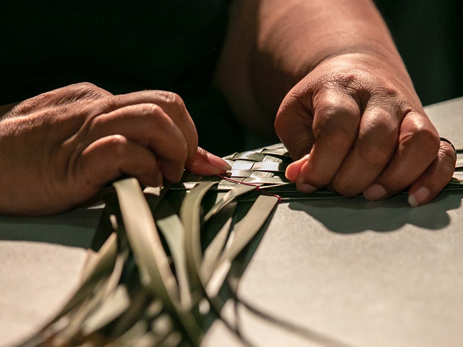 Power to the Puoro, 2021. Photo by Jo Moore. Te Papa (181511) Two hands weaving green flax on a table.