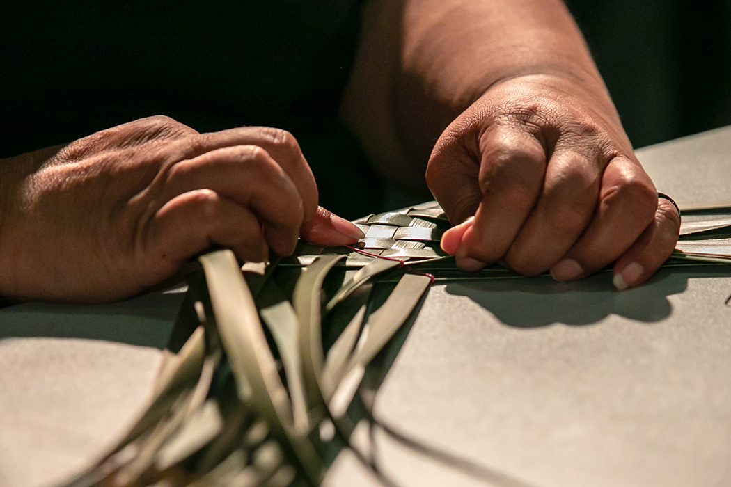 Two hands weaving green flax on a table.