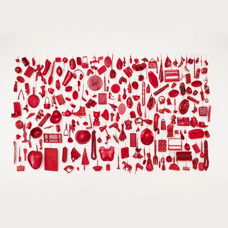 A mural of a large number of objects, ranging from headphones to an egg beater, dipped in red wax