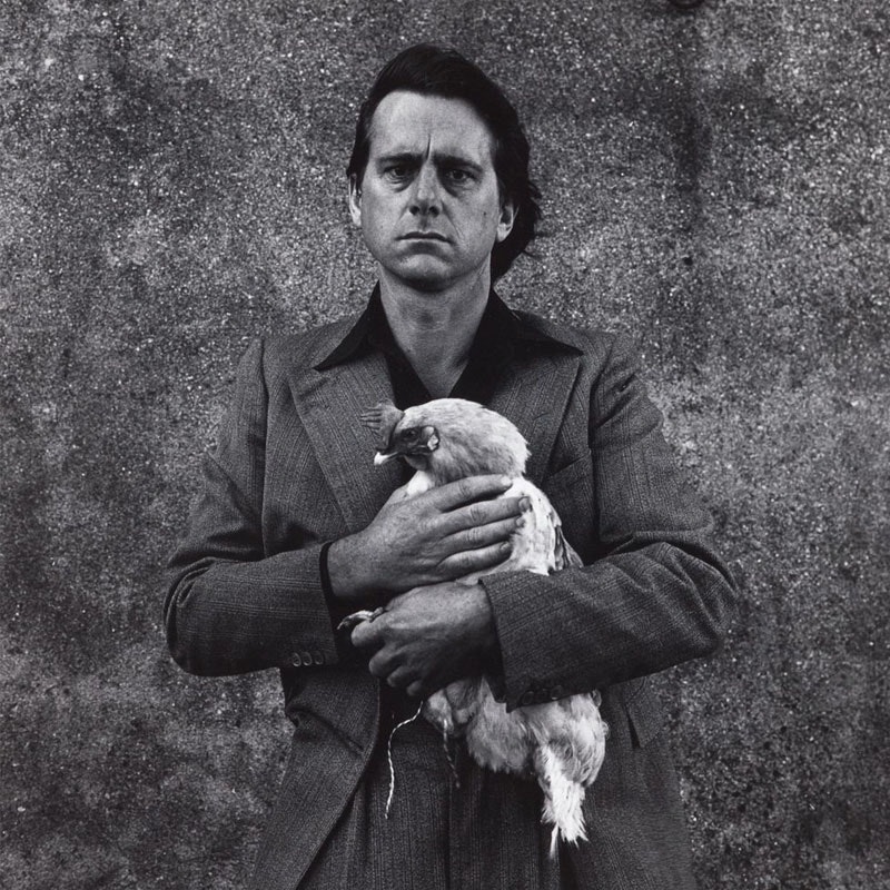 Man (Peter Peryer) wearing a jacket and black shirt holding a rooster