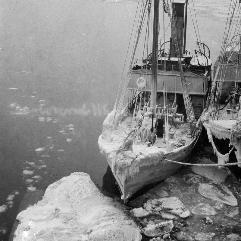 A black and white photo of a fishing boat surrounded by ice, there's ice covering the boat too