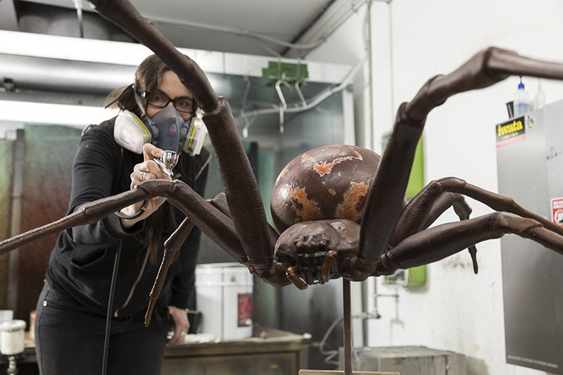 A lady sprays a giant model spider with paint