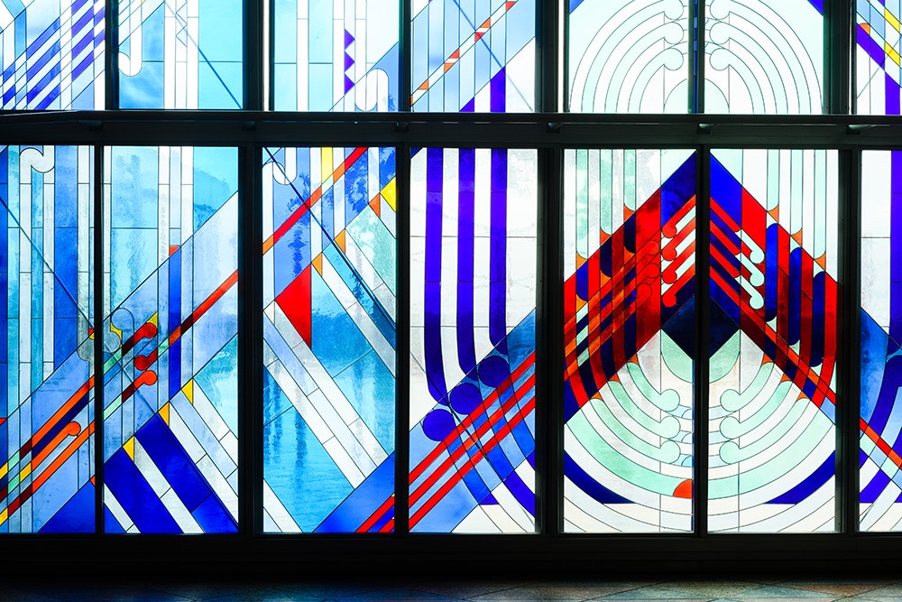 Stained glass window with red and blue lines, symbols and shapes.