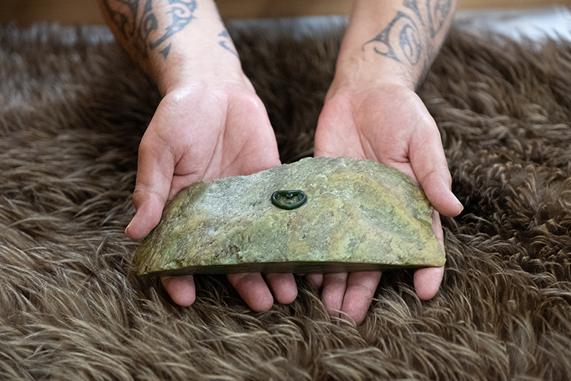 Twp hands holding a large piece of pounamu