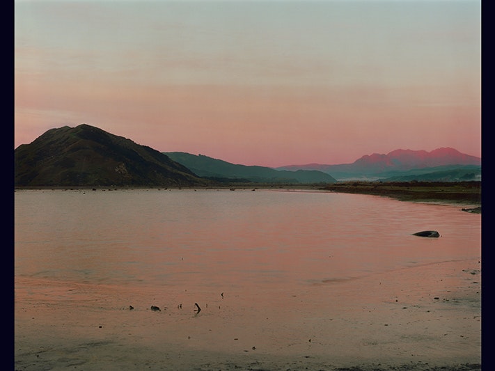 Image credit line: Natalie Robertson, A Red-Tipped Dawn — Pōhautea at Waiapu Ngutu Awa (7th August 2020) 2020, colour photograph. Te Papa (O.049752) A photograph of a a sunset on the mouth of a river. The sunset is reflected in the smooth water.
