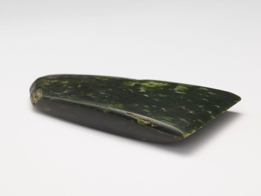 A greenstone adze sitting on a white background.