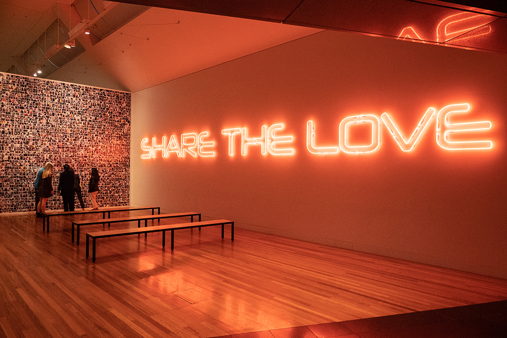 A large wall with large neon sign that says Share the love.