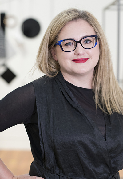 A woman with long blond hair and glasses is smiling at the camera.