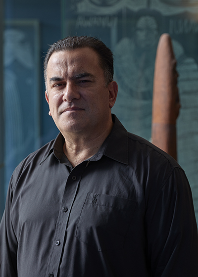Head and shoulders of a man looking at the camera. He is half in shadow,