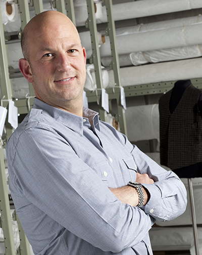 A man with no hair is looking side on at the camera. He has his arms folded