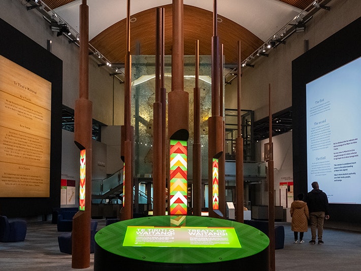 Te Tiriti o Waitangi: Ngā tohu kotahitanga, 2024. Photo by Jane Harris. Te Papa (244624) A space in a museum with tall poles and two walls with text on them.