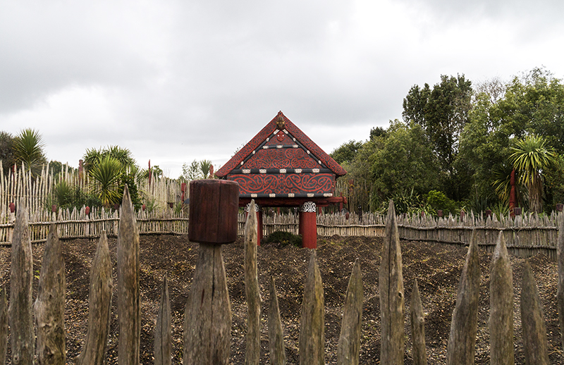 A small red and black hut on stilts in a garden of dirt shaped in small mounds.