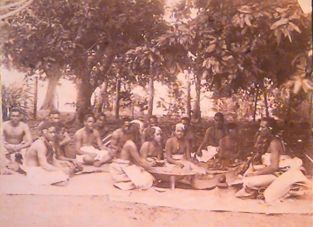 Sepia image of 15 people sitting on flax mats under trees