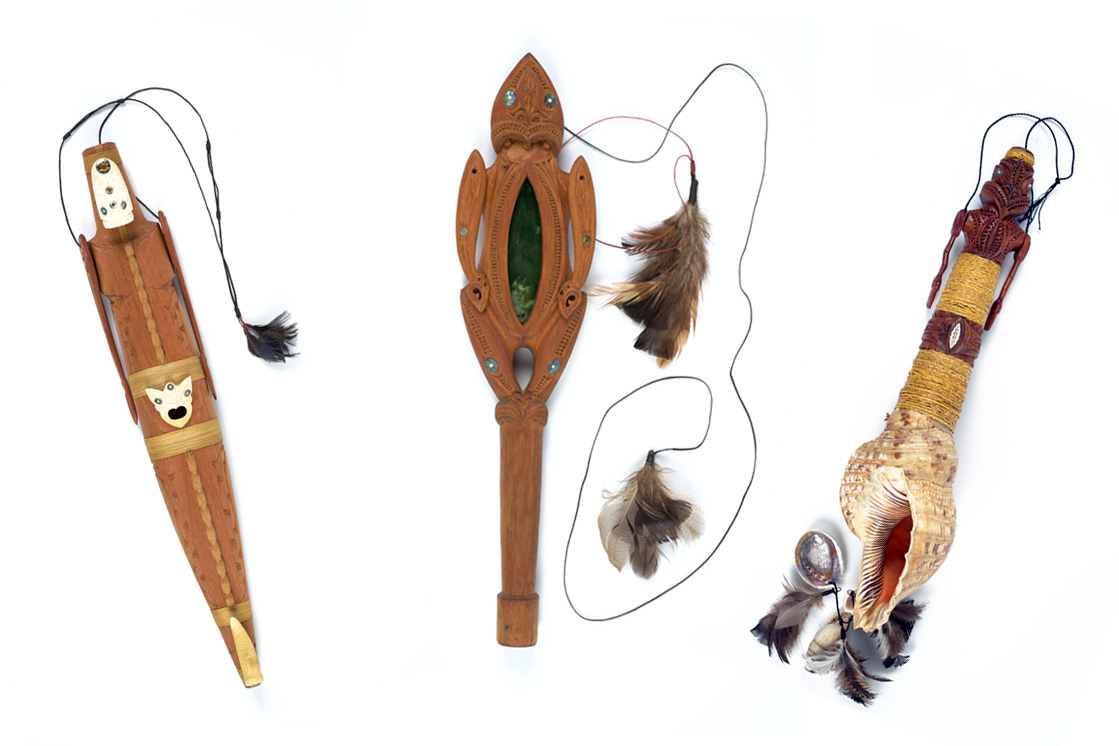 Three carved wooden marionettes with cords and feathers attached on a white background.