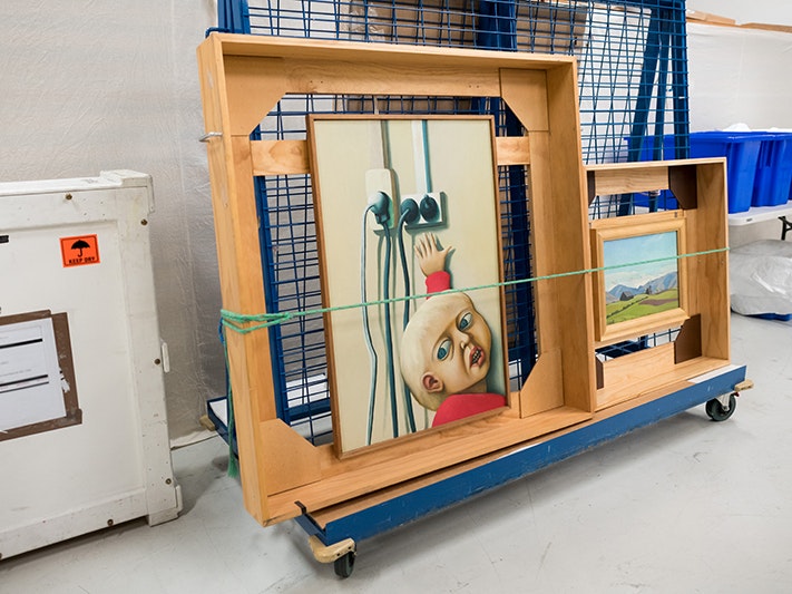 Te Papa art store. Photo by Mark Tantrum Photography, July 2019. Te Papa (145281) A rack on wheels in a store room – the rack has two art paintings tied on with strops.