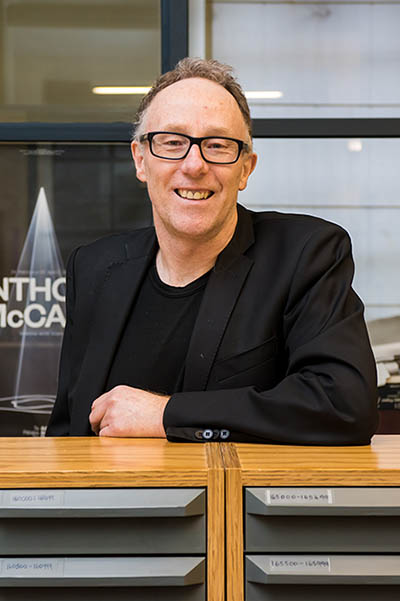 A head and shoulders photo of a man leaning on a file cabinet and smiling at the camera
