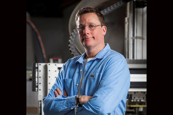 A man in a blue shirt with his arms crossed is looking at the camera.