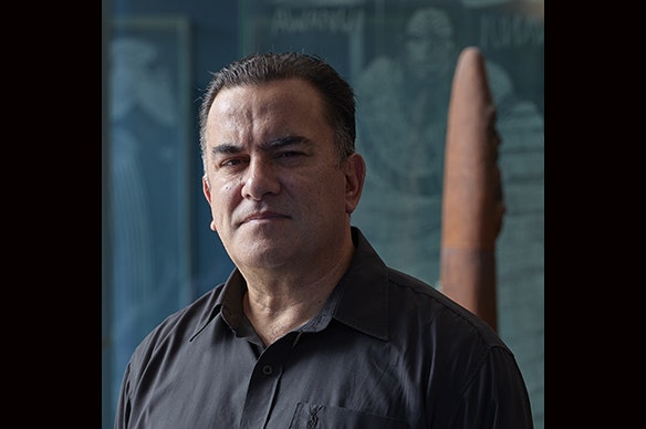 Head and shoulders of a man looking at the camera. He is half in shadow,