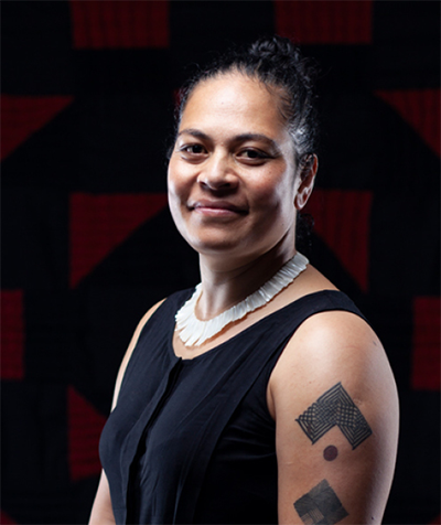 Head and shoulders of a woman turned one-quarter to the camera. She has short sleeves and a tattoo on her arm