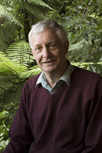head and shoulders photo of a man with white hair. He is sitting in front of an image of ferns