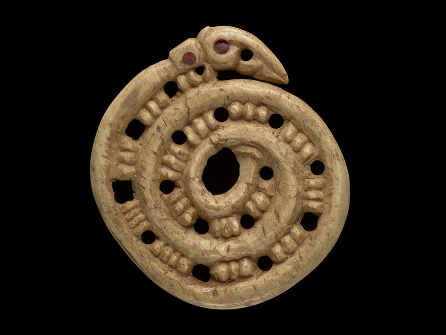 Koropepe (pendant), Unknown carver, whale bone (bone), wax, 1850–1900; New Zealand. Purchased 1907. Te Papa (ME001654) A spiral carving with holes every four notches. There is a ahead at the end of the spiral with red beads for eyes. He whakairo tōrino whai kōhao i ia whā pākati. Kei te pito o te tōrino tētahi upoko whai pirepire whero hei karu.