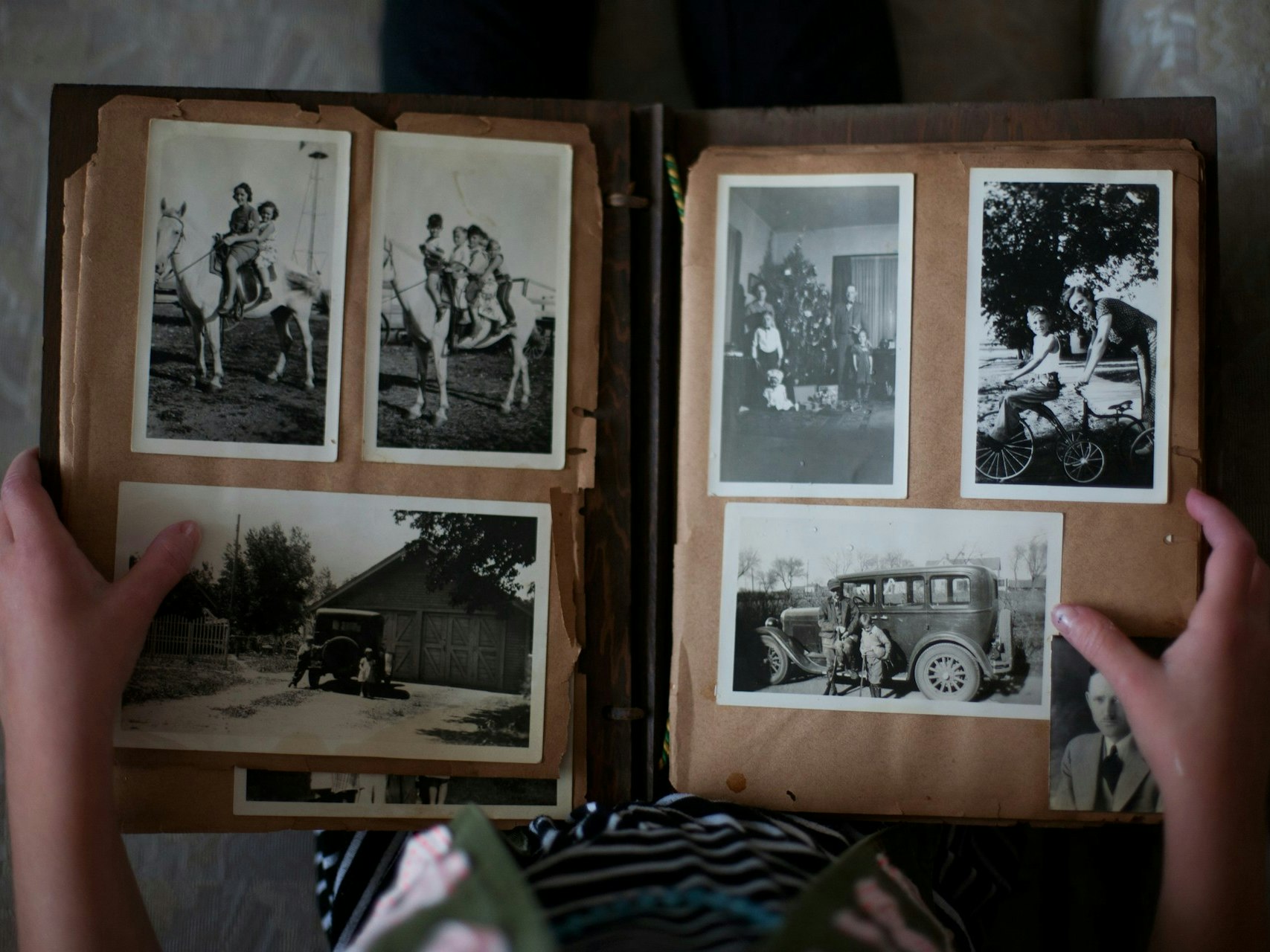 Photo by Laura Fuhrman on Unsplash a top-down photo of an open photo album with six black and white photos of people in the page spread. There are two hands holding the album open.