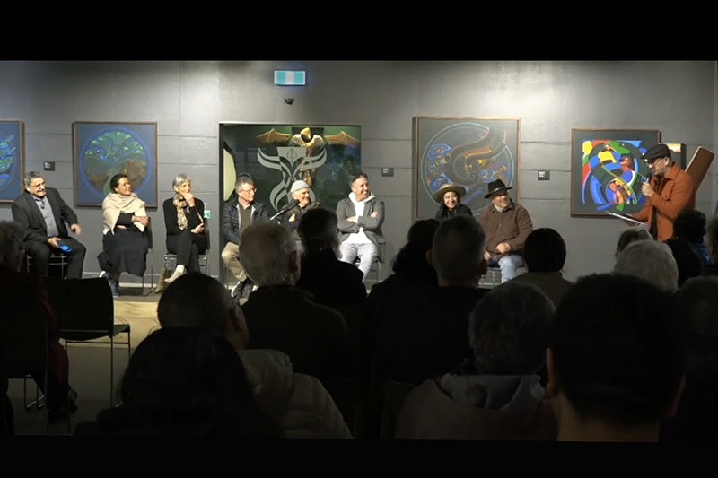 Still from Turanga FM video of Te Maori panel talk. Eight people are sitting in front of an audience while one man is standing at the end talking to them. They are all smiling.