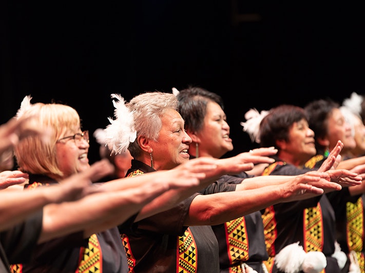 Matariki Festival 2018. Taranaki ki Te Tonga Taikura performing at Taikura Kapa Haka event, 2018. Photograph by Jo Moore. Te Papa (108393) Several older women are performing on stage. They are all facing the same direction with their arms up at shoulder level.