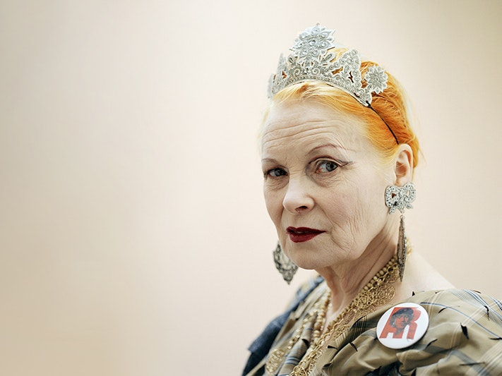 Vivienne Westwood: Photo © Jo Metson Scott A long beige banner image with an older woman with bright orange hair, heavy makeup, a tiara and bold jewellery on. She is looking at the camera with a slight sneer.