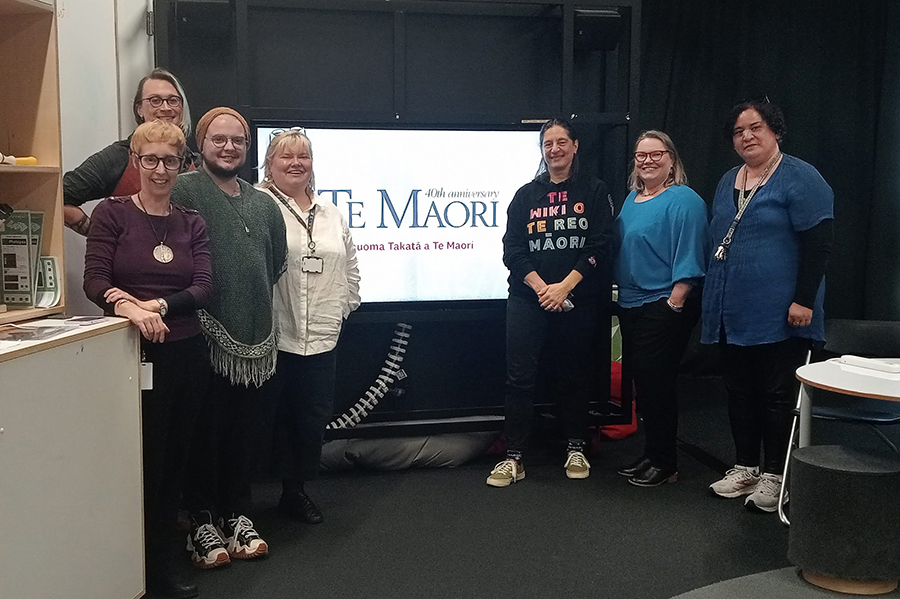 Seven people standing in front of a screen with the words Te Māori 40th anniversary on it.