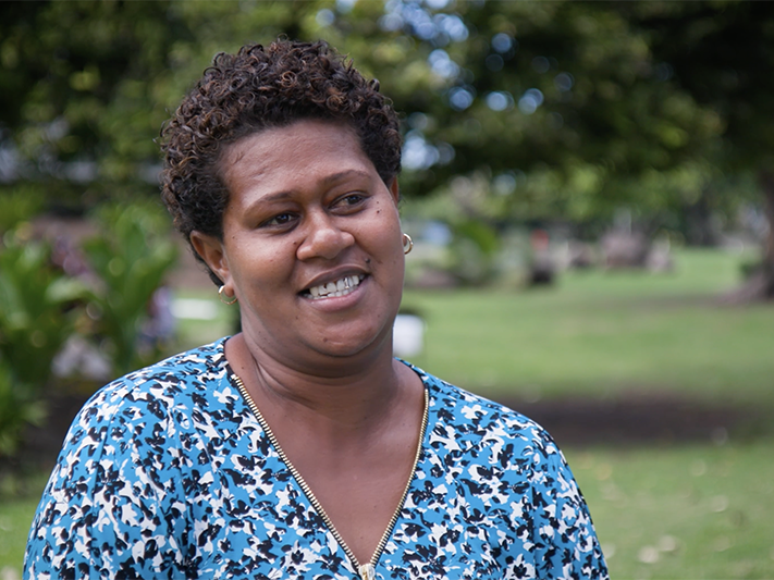 Still from the interview with Liviana. Te Papa A woman is standing outside and smiling. She is talking to someone off camera.
