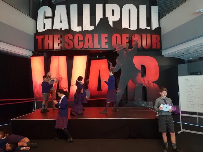 Students from Our Lady of Victories School respond to Gallipoli: The Scale of Our War using 3D scanning, 2018. Photo by Jessie Robieson. Te Papa Several children in school uniform are milling about the front entrance to the exhibition Gallipoli The Scale of Our War at Te Papa.