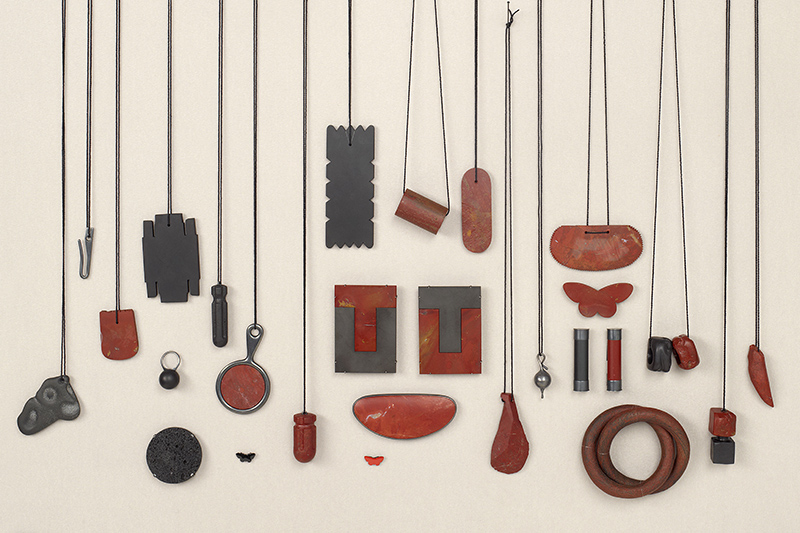 A spread of different pieces of jewellery made by the same jeweller. Most of them are hanging on dark threads.